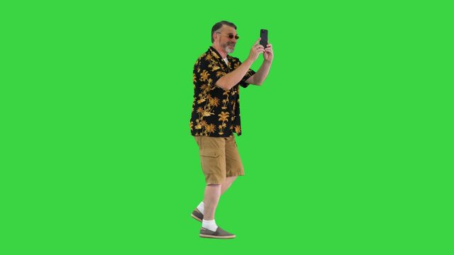 Happy senior bearded tourist man walking and taking pictures with his phone on a Green Screen, Chroma Key.