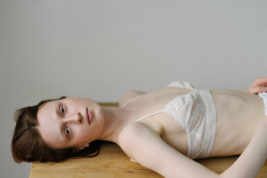 beautiful red-haired model in a white bra is lying on the table