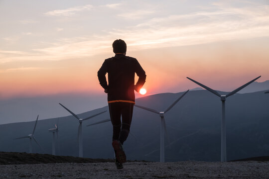 man running towards wind generators in the setting sun - Powered by Adobe