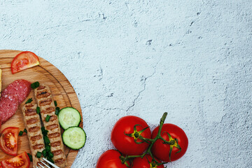 Fresh vegetables: tomatoes, cucumbers, sliced, boiled sausage and hunting sausages on a plate on a wooden background. Tableware. The view from the top, place for text.
