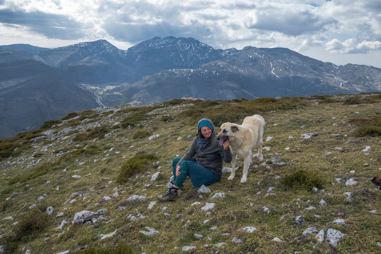 a woman and a big guard dog enjoy a moment on top of a mountain.