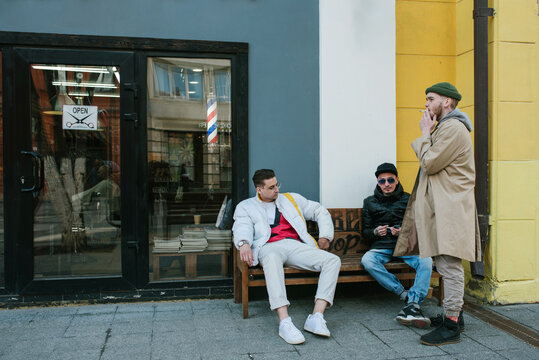 Guys sit and smoke on a bench on the street near the barbershop