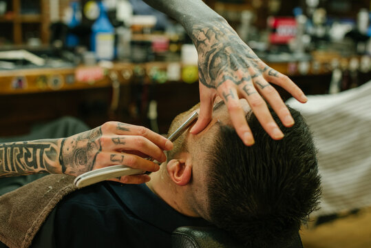 Closeup photo of a barber&sbquo;&Auml;&ocirc;s hands Shaving a dark hair guy with a razor