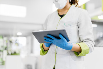 Unrecognizable female pharmacist using tablet wearing gloves and face mask
