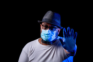 Black man with blue gloves and face mask says stop with black background.