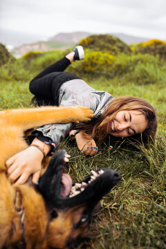 Laughing woman with dog on green meadow in hills