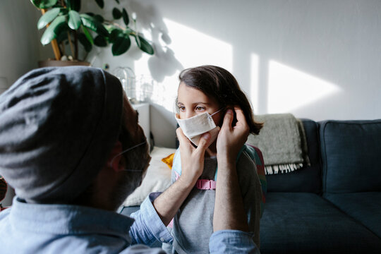 Father putting face mask to his daughter at home