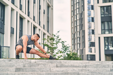 Fototapeta na wymiar Man runner kneading his legs doing stretching before training while standing on the stairs in the street. Sport concept