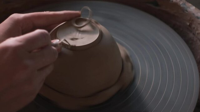 Close up of hands working clay on potter's wheel. Potter shapes the clay product with pottery tool. Handmade Background