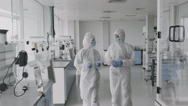 Scientist walking in laboratory wearing protective coverall discussing science experiment test results
