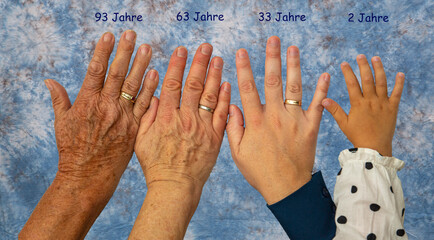 Vier Hände im Alter von jeweils 93 Jahren, 63 Jahren, 33 Jahren und 2 Jahren vor einem blau...