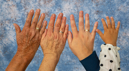 Vier Hände im Alter von jeweils 93 Jahren, 63 Jahren, 33 Jahren und 2 Jahren vor einem blaum...