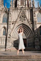 Full body low angle of elegant young ballerina in dress standing on tiptoe while performing sensual dance against aged stone cathedral