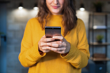 Cropped unrecognizable happy young female in casual outfit using mobile phone while standing on modern loft room