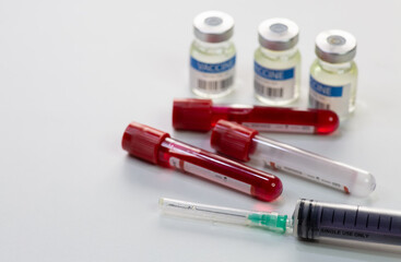 Injection syringe with blood sample vials of patients and vaccine bottles on white background