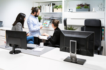 Young male manager holding tablet with diagrams and analyzing financial results of business project during meeting with female coworkers in modern workspace