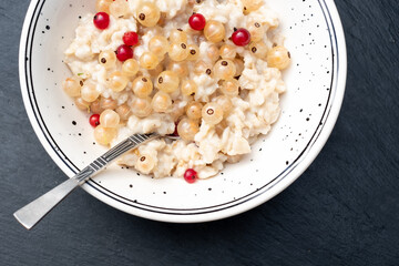 Healthy vegetarian breakfast bowl with whitecurrants and redcurrants. Oatmeal porridge with fresh berries mix on black stone background. Kids menu.