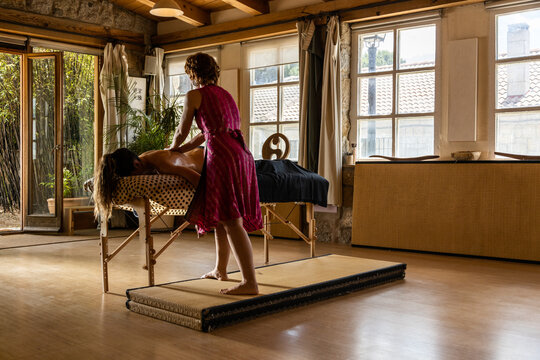 Back view of professional female therapist doing ayurvedic massage with essential oil on back of to relaxed woman in spa salon