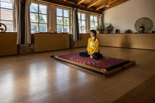Calm female in sportswear sitting on mat in spacious studio and practicing yoga in Padmasana meditation
