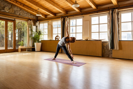 Flexible female in sportswear standing in Triangle pose in spacious studio while practicing yoga and looking up