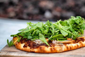 Closeup of flatbread pizza topped with arugula, pine nuts, pepper and various cheeses