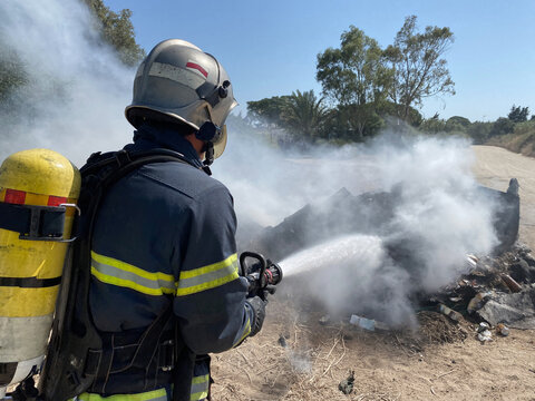 Back view of brave fireman in protective uniform standing with hose and extinguishing fire on dump in nature