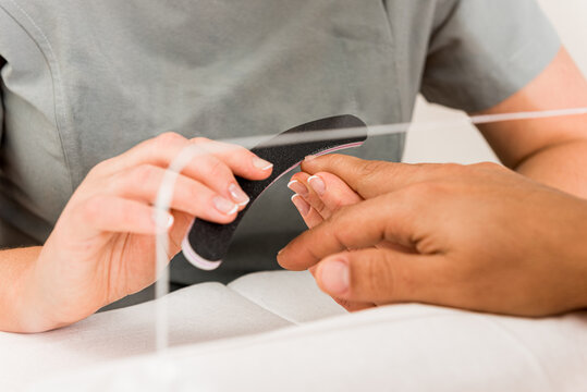 Cropped unrecognizable female specialist doing professional manicure procedure in cropped anonymous male in modern beauty center