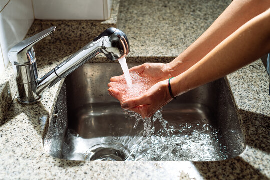 Unrecognizable person cleaning hands with water while standing near sink in bathroom lit by sunlight