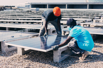 Busy black male engineers installing solar batteries in construction site of modern factory during sunny day