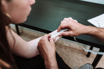 High angle of unrecognizable male master measuring part of arm of female customer for applying tattoo