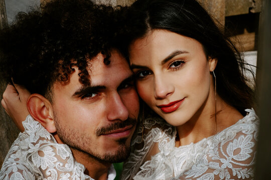 High angle of sensual newlywed couple in stylish clothing cuddling gently while standing on wooden bridge looking at camera