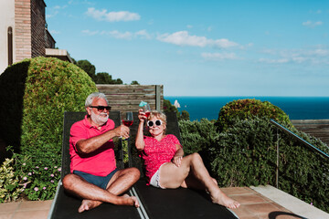 High angle of relaxed senior couple lying on loungers on terrace and drinking refreshing tropical cocktails while enjoying summer holiday