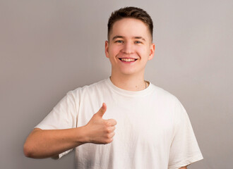 Young smiling handsome worker in formal clothing demonstrating thumb up against gray background