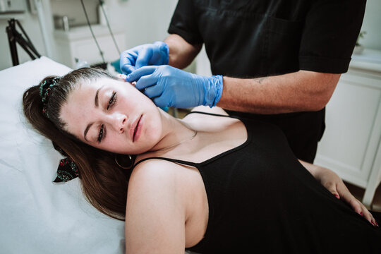 Tattooist making marks on ear of female customer before applying tattoo during work in modern salon
