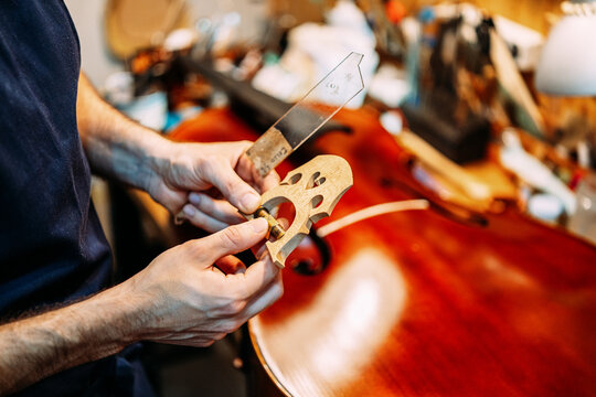 Side view of crop anonymous male master holding violin bridge and professional tool while building musical instrument in workshop