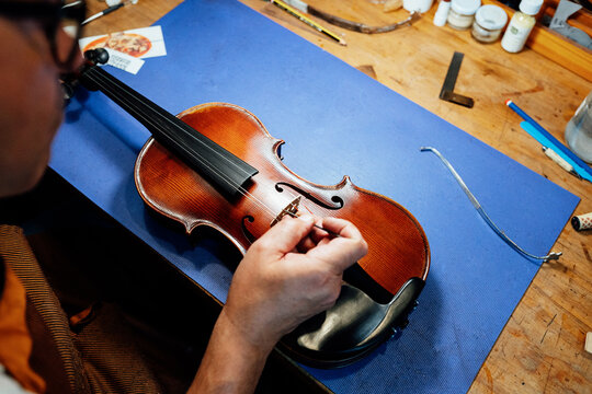Crop unrecognizable male artisan master setting bridge on violin after replacing strings during restoration work in workshop