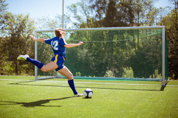 Side view of unrecognizable female athlete shooting ball into goal while playing football on field