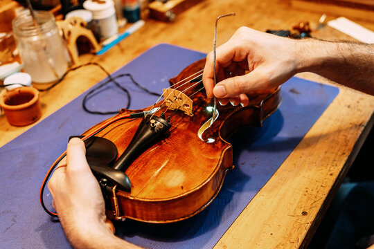 Crop anonymous craftsman setting sound post while building string instrument in workshop