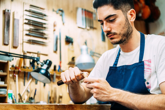 Serious young artisan luthier processing hair for violin bow with professional tool while working in workshop