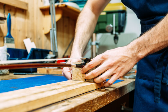 Crop anonymous craftsman inserting violin bow into wooden holder while repairing musical instrument in workshop