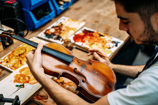 Side view of crop anonymous craftsman painting antique violin during restoration work in workshop