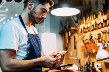 Side view of skilled young craftsman fabricating violin bridge while working in professional workshop