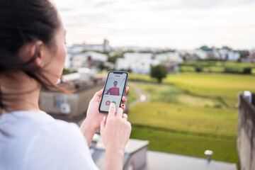 Anonymous woman selecting man while resting on terrace and browsing dating app on smartphone