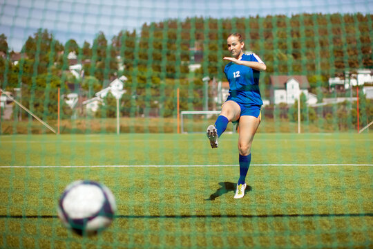 Female athlete shooting ball into goal while playing football on field