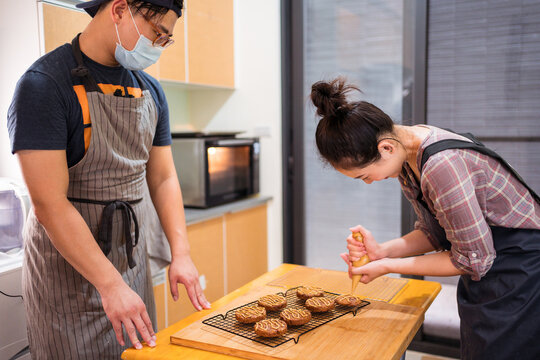 Modern ethnic man and woman in aprons in kitchen making chocolate chip biscuits with caramel sauce