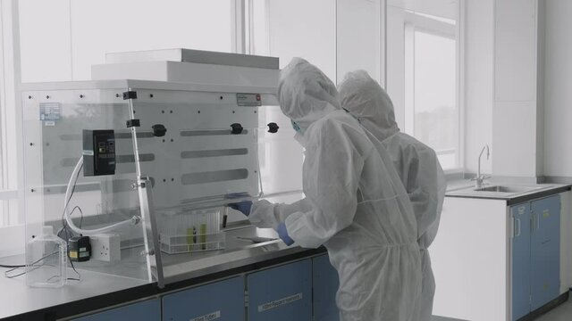 Scientist walking in laboratory wearing protective coverall discussing science experiment test results