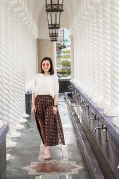 Ethnic female traveler in summer outfit standing in ornamental walkway with stone columns of Omar Ali Saifuddien Mosque during holiday and looking at camera
