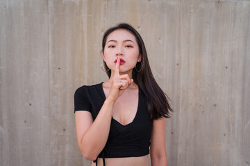 Calm Asian female standing with index finger on lips and demonstrating hush sign while looking at camera