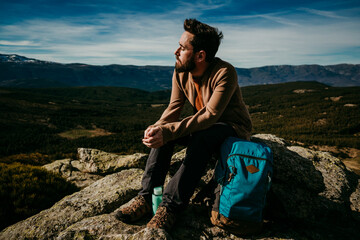 Optimistic man resting sitting on stones with eyes closed near backpack while enjoying the moment in Puerto de la Morcuera mountains on cloudy day in Spain