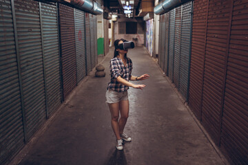 Calm female standing on narrow shabby street and experiencing virtual reality while wearing wireless VR goggles